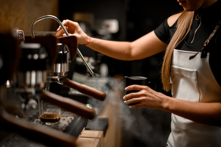 female barista turns on coffee machine that releases steam to make Puerto Rican coffee drink